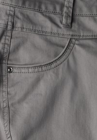 Tissu en coton gris montrant un gros plan d'un détail de poche avec des coutures et un bouton en métal. Texture lisse, design décontracté.