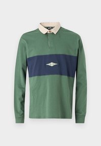 Dlhý rukáv polo tričko v zelenej a námořníckej farbe, s kontrastným béžovým golierom a horizontálnou panelou s vyšitým logom. Vyrobené z bavlny.