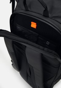 Sac à dos noir avec un extérieur lisse et durable. Caractéristiques : un onglet orange, plusieurs compartiments internes et un soutien dorsal rembourré.