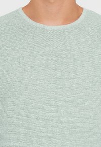 Ανοιχτό πράσινο πλεκτό πουλόβερ με στρογγυλή λαιμόκοψη. Διαθέτει υφασμάτινη υφή και μαλακή, αναπνεύσιμη εμφάνιση.