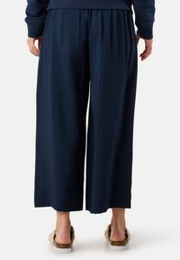 Marineblaue weite Hosen aus einem strukturierten Stoff, mit einem gerafften Bund und kombiniert mit hellfarbigen Sandalen.