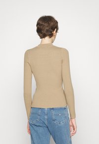 Haut beige à manches longues côtelé avec un col montant, une coupe ajustée et un tissu texturé, associé à un jean taille haute bleu clair.
