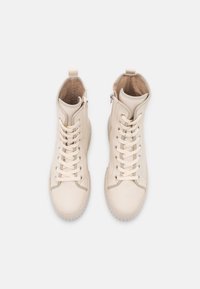 Zapatillas de deporte de caña alta beige con un exterior de cuero suave, cordones planos, cuello acolchado y un zipper lateral. Suela de goma con agarre texturizado.