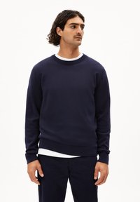 Marineblauwe crewneck sweatshirt van een zachte knitstof met ribgebreide boorden en zoom, gedragen over een wit T-shirt. Eenvoudig, klassiek ontwerp.
