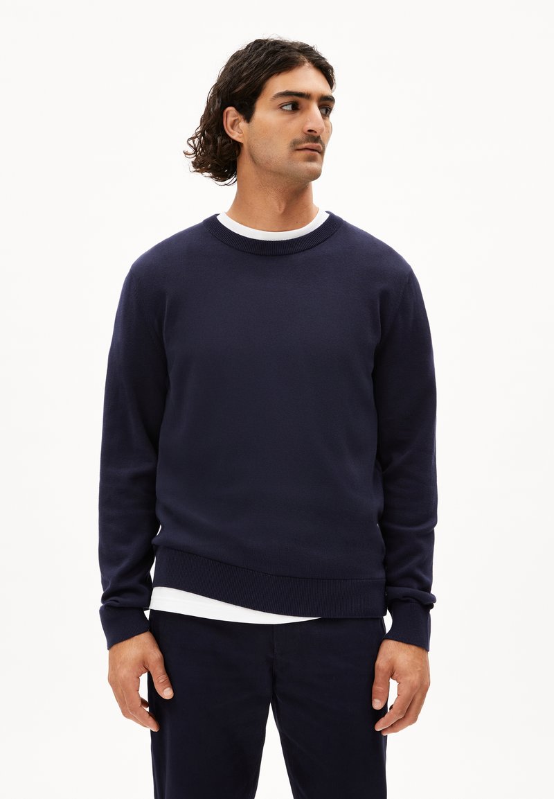 Marineblauwe crewneck sweatshirt van een zachte knitstof met ribgebreide boorden en zoom, gedragen over een wit T-shirt. Eenvoudig, klassiek ontwerp.