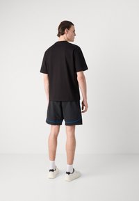 T-shirt di cotone nero, maniche corte, abbinato a pantaloni corti neri con accenti blu, indossato con calze bianche e sneakers. Design semplice.