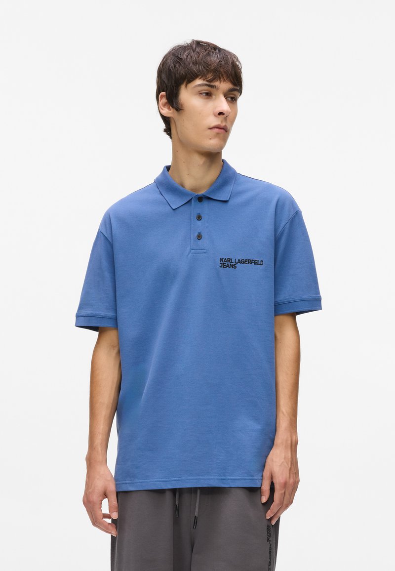 Μπλε πουκάμισο polo φτιαγμένο από βαμβάκι, με κλασικό γιακά, δύο κουμπάκια στο μπροστινό μέρος και κεντημένο λογότυπο "Karl Lagerfeld Jeans" στο στήθος.
