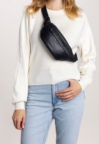 Černá kožená kabelka přes tělo s elegantním designem, zakřiveným tvarem a nastavitelným popruhem. Obsahuje zipové uzavírání a hladký povrch.