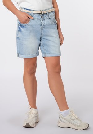 Lichtblauwe opgerolde denimshorts met gevlochten beige riem, gedragen met witte sneakers en enkelsokken bij een staand persoon.