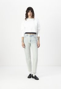 Sweatshirt branco curto com ombros caídos, combinado com jeans de cintura alta azul claro. Mocassins pretos completam o look.
