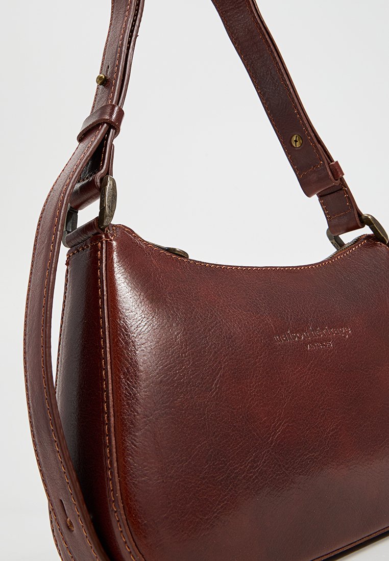 Braune Leder-Schultertasche mit geschwungenem Design, verstellbarem Tragegurt und dezenten Nähdetails. Sie hat eine glatte Textur und eine polierte Oberfläche.