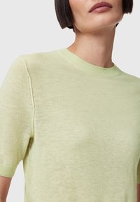 Lichtgroene sweater met korte mouwen en een ronde halslijn, zachte textuur en subtiele glans. Een opmerkelijk detail is de gebreide ribbelkraag.