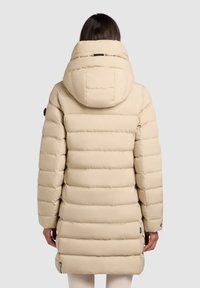 Béžová puff jacket s vysokým golierom a kapucňou, so zvýrazneným horizontálnym prešívaním a elastickými manžetami; vystavuje hladký, textúrovaný povrch.