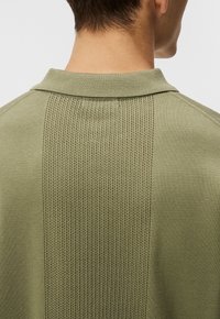 Polo vert avec un panneau arrière texturé et un col lisse. Présente un motif en tricot contrasté le long de la colonne vertébrale, créant un intérêt visuel.