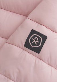 Ljusrosa pufferjacka med horisontellt quiltat mönster. Har en distinkt svart logotypklistermärke i det övre hörnet. Mjuk textur.