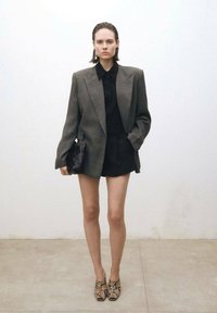 Szary oversize blezer na czarnej bluzce i szortach. Nosi się go z butami na obcasie w wężowy wzór oraz teksturowaną czarną kopertówką.