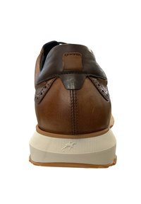 Bruine leren schoen met een contrasterende donkerbruine hak, voorzien van brogue-detaillering en een gestructureerde witte rubberen zool.
