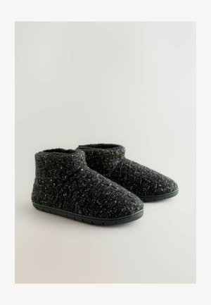 Pantoufles noires arrivant à la cheville, fabriquées en tissu texturé avec un motif moucheté, dotées d'une semelle en caoutchouc flexible et d'un design à bout arrondi.