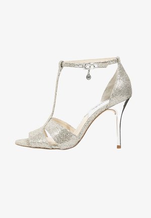 Srebrne brokatowe sandały na wysokim obcasie z otwartym noskiem, z paskiem T, zapięciem na kostkę i metalicznym akcentem na obcasie. Teksturowane wykończenie z brokatowym połyskiem.
