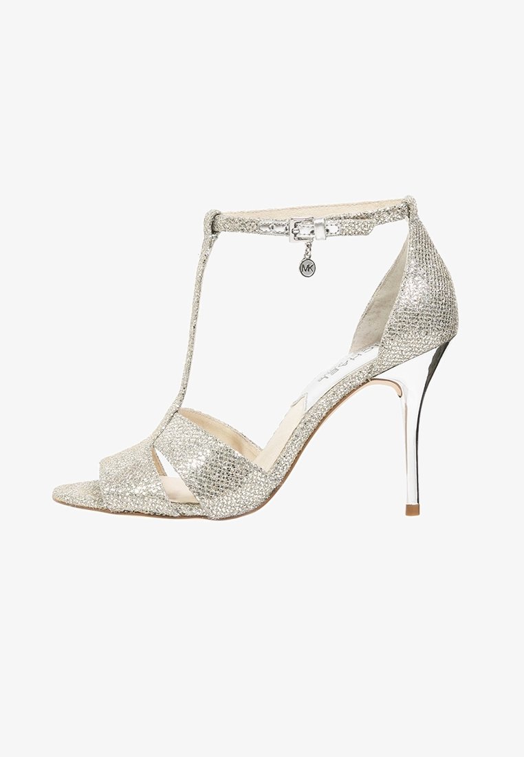 Sandale à talons hauts en paillettes argentées avec un bout ouvert, design à tige en T, boucle à la cheville et accent métallique sur le talon. Finition à paillettes texturées.