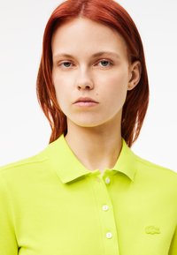 Koszulka polo Lacoste w jasnym limonkowym kolorze, z kołnierzykiem, listwą guzikową i haftowanym logo na piersi. Teksturowany materiał.