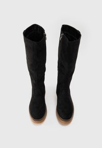Bottes noires en daim à hauteur de genou avec un bout rond, fermeture éclair sur le côté et semelle en caoutchouc beige. Présente des coutures tonales et une finition texturée.