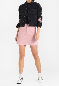 Black denim jacket with rose embroidery on sleeves, paired with a pink corduroy skirt. White sneakers complete the outfit.