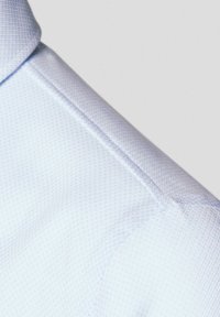 Jasnoniebieska, teksturowana kołnierzyk koszuli z subtelnym wzorem diamentowym, gładki materiał i staranne szycie na krawędzi.