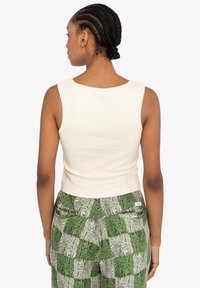 Cremefarvet, ærmeløs cropped top med en glat tekstur, parret med grønne mønstrede bukser med skiftende firkantede designs.