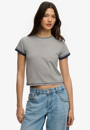 Kvinde iført en grå kort T-shirt med marineblå kant på ærmer og krave, kombineret med lyseblå, højtaljede jeans.