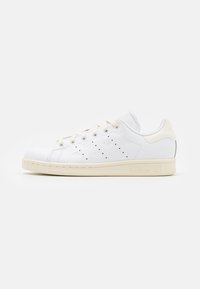 Zapatilla blanca de cuero con detalles perforados, suela de goma color crema, cordones en la parte delantera y branding en relieve en el lateral y el talón.