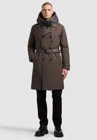 Brown trench coat with a detachable gray hood, double-breasted design, belted waist, and side pockets, styled with black pants and shoes.