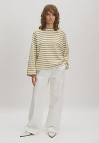 Gestreepte lange mouw top in crème en beige, met een ronde halslijn en een ontspannen pasvorm, gecombineerd met witte wijde broek en puntige schoenen.