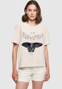 Lyserød T-shirt med korte ærmer, der har et stort sort sommerfuglegrafik og stiliseret tekst. Blødt materiale, afslappet pasform.