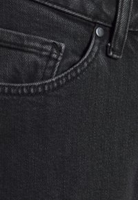 Vaqueros de denim negros con una textura sutil, que cuentan con un bolsillo delantero, botón metálico y costuras en contraste a lo largo de las costuras.