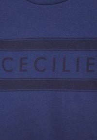 Modrá bavlněná mikina s výraznými tmavě modrými horizontálními pruhy a slovem "CECILIE" umístěným uprostřed v moderním bezpatkovém písmu.