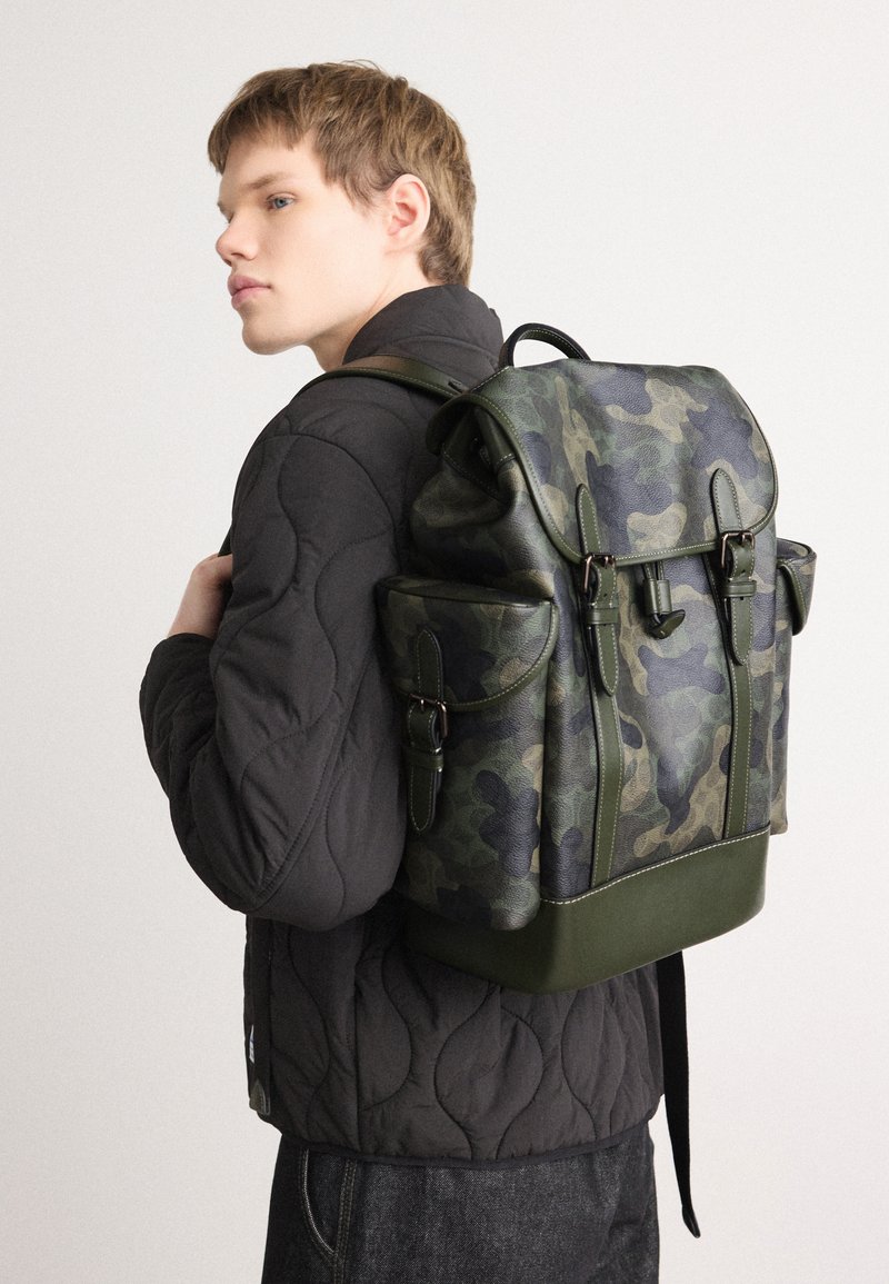 coach camouflage backpack men green multi Outlet West In Signature Camo Print Signature coated canvas and smooth calf leather Inside zip cell phone and multifunction pockets Inside tech sleeve Drawstring and speedclip closures fabric lining Top handle with 2 1/4 drop Outside zip and slip pockets Outside zip access to interior Adjustable shoulder straps 10 1/2 (L) x 16 1/2 (H) x 6 (W) Style No. Coach West Backpack In Signature