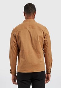 Beżowa bawełniana kurtka z długimi rękawami, mankietami na guziki i casualowym kołnierzem, cechująca się minimalnymi przeszyciami oraz gładkim, teksturowanym wykończeniem.