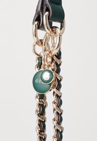 Grøn læderrem med gul hardware og sammenflettet kædedesign. Har to runde mærker med teksten "G" og "GUCCI". Glat tekstur.