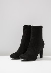 Bottes basses en daim noir à texture lisse, bout arrondi, fermeture éclair latérale, et talon aiguilles de 5 pouces.