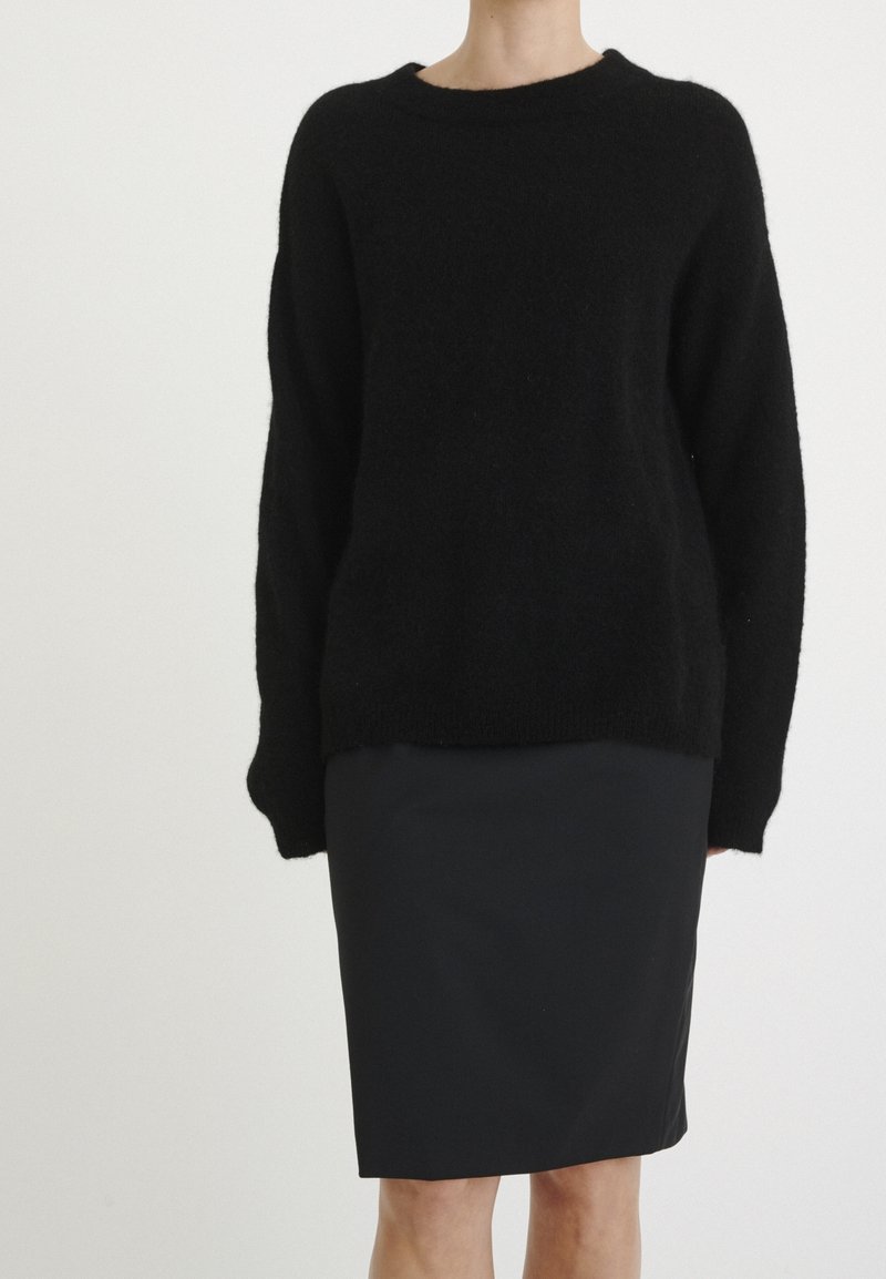 Svart tröja i mjuk, fluffig stickning, med rund halsringning och långa ärmar, matchad med en figurnära svart blyertskjol.