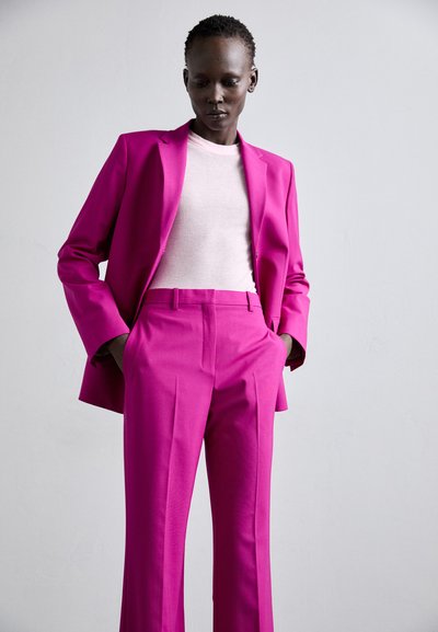 Vaaleanpunainen räätälöity puku, jossa on muotoiltu bleiseri ja suorat housut, yhdistettynä vaaleanpunaiseen slim fit -paitaan. Sileä kangasviimeistely.