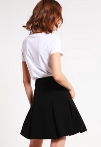 Mustat poimu hame, jossa on istuva vyötärö, valmistettu kevyestä kankaasta. Yhdistetty valkoiseen lyhythihaiseen t-paitaan.