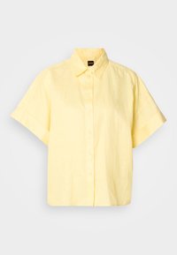 Chemise jaune clair à manches courtes avec col et étiquette noire portant la mention "BOSS" au niveau du col.