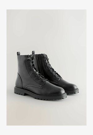Zwarte leren enkellaarzen met een vetersluiting aan de voorkant, een ritssluiting aan de zijkant, een gestructureerde zool en versterkte stiksels langs de randen.