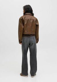 Giacca cropped in pelle marrone con una texture liscia e colletto, abbinata a pantaloni larghi in denim scuro a vita alta.