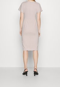 Knälång, figurnära klänning i ljusbeige tyg med korta ärmar och dragkedja bak. Parat med svarta öppna klackar.