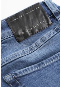 Dżinsy denimowe w jasnoniebieskim kolorze. Posiadają czarną skórzaną metkę z wytłoczonym napisem "bugatti" oraz białe szwy na kieszeniach.