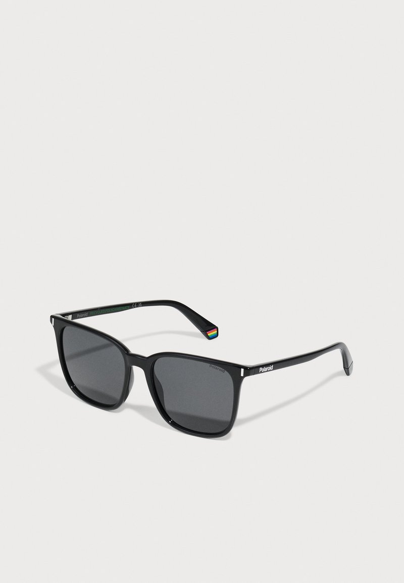 Black rectangular sunglasses with dark lenses, plastic frame, and subtle rainbow accent on the tip of the arm. Polaroid branding on the side.
