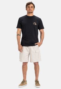 Camiseta de algodón azul marino con un pequeño logo marrón claro en el pecho, combinada con pantalones cortos cargo beige con grandes bolsillos y un corte relajado.